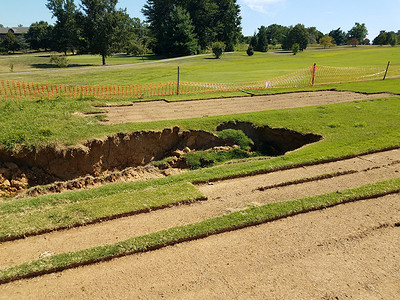 土壤侵蚀摄影照片_高尔夫球场草地和泥土中的天坑或侵蚀