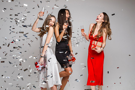 三个女孩在五彩纸屑下喝酒玩得很开心。