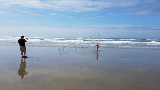 父亲在海滩的沙子和水中给儿子拍照