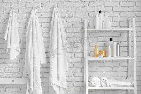 带化妆品瓶的浴室搁架和挂在白砖墙上的毛巾