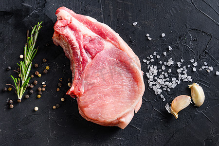猪排骨摄影照片_有机排骨或五花肉新鲜生肉，配以香料、迷迭香和红辣椒，位于黑色石板上。