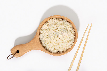在白色背景上用木勺和筷子煮熟的米饭。