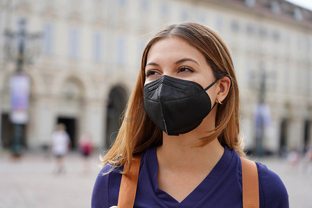 戴着KN95 FFP2防护黑色口罩走在城市街道上的女学生画像