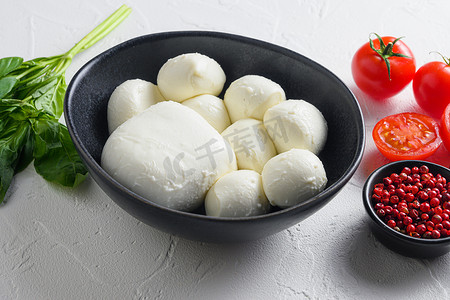 生熟马苏里拉奶酪球，配有新鲜罗勒叶和樱桃番茄，配料，白色背景