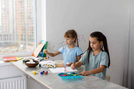 玩颜料的孩子摄影照片_桌边的两个小女孩拿着画画的颜料