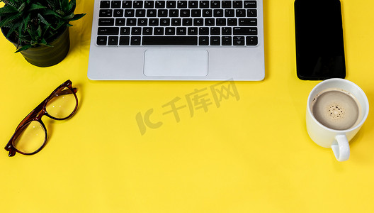 工作区桌面摄影照片_笔记本电脑放置在商业工作场所的黄色桌子背景上，配有一杯咖啡，空工作区