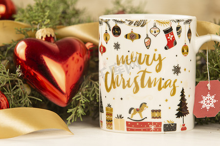 圣诞杯的特写，上面挂着空茶标签，周围有松枝、红色小饰品和缎带金丝带，带有散景效果