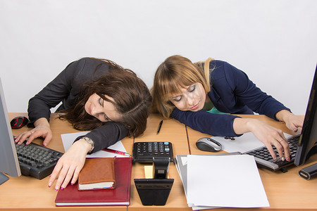 两名年轻的办公室员工在电脑桌上睡着了