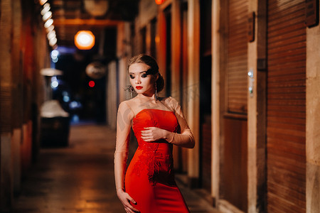红色晚礼服摄影照片_夜城马赛街头，一个穿着红色晚礼服的优雅女孩。法国一个穿着红色晚礼服的女人