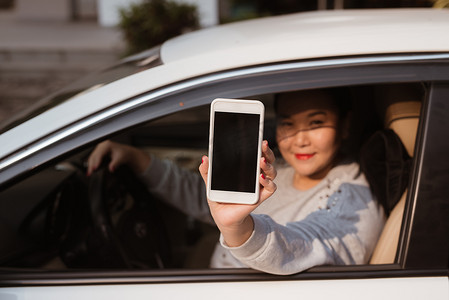 有魅力的年轻女人在车展与空白屏幕的智能手机。