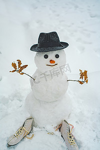 滑稽的雪人用胡萝卜而不是鼻子，在模糊的雪地背景下，在白雪皑皑的草地上戴着一顶温暖的针织帽子。