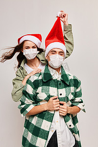 一个穿格子衬衫的男人和一个戴着医用面具、头戴节日帽的快乐女人