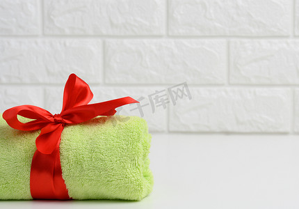 在浴室的白色架子上卷起用红色丝带绑着的特里绿色毛巾，复制空间
