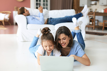 科技摄像头摄影照片_快乐的妈妈和小女孩看着屏幕笔记本电脑，与网络摄像头交谈，通过计算机应用程序在线聊天。
