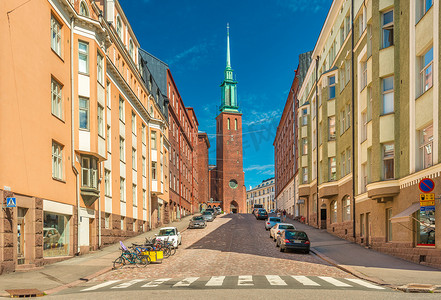 赫尔辛基教堂摄影照片_赫尔辛基 — 2019 年 6 月，芬兰：一条拥有传统建筑和新哥特式瑞典教堂 (Kristuskyrkan) 的街道