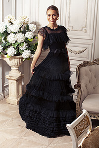 身穿黑色蕾丝时尚风格连衣裙的年轻漂亮女士在皇家酒店房间的丰富内饰中摆出姿势，奢华的生活方式人们的概念