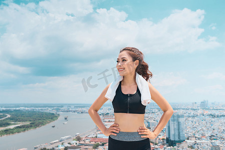 微笑着穿着运动服的年轻女子站在屋顶上，俯瞰着蓝天。