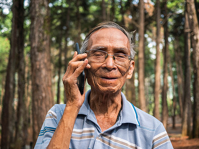 亚洲老人在花园里使用智能手机。