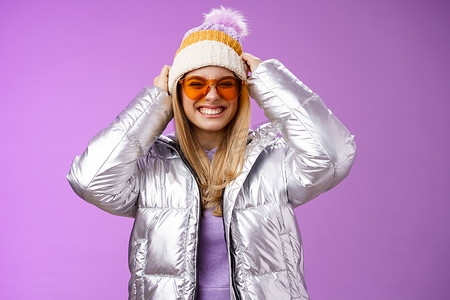 精力充沛、大胆时髦的年轻迷人女性，在冬季旅行中与朋友玩得开心，学习单板滑雪，面带微笑，享受假期，戴上银色保暖夹克太阳镜，紫色背景