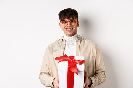 英俊的年轻人做礼物，拿着礼物盒，对着镜头微笑，站在白色背景上