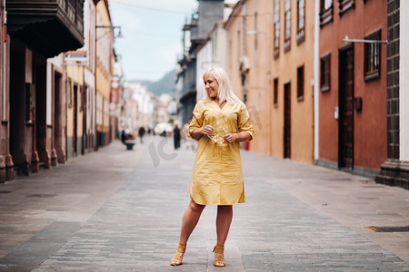一位身穿黄色夏装的金发女子站在特内里费岛拉古纳老城的街道上。西班牙，加那利群岛