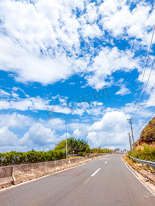在阳光明媚的夏日，蓝色多云的天空，有混凝土屏障和标线的干沥青空车路。