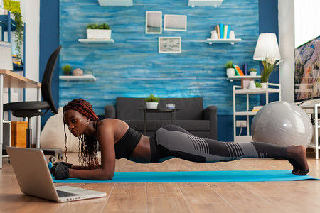 穿着紧身裤、坐在瑜伽垫上做平板姿势的运动型黑人女性