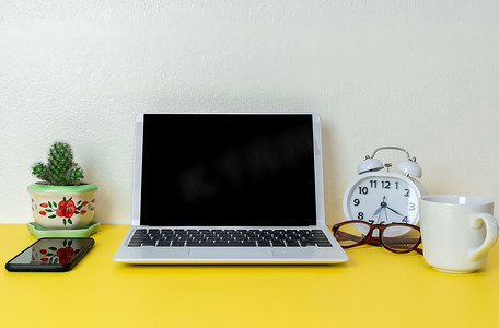 笔记本电脑放置在商业工作场所的黄色桌子背景上，配有一杯咖啡，空工作区