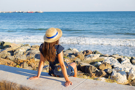 戴帽子的漂亮女孩坐在海边的石头上