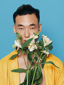 韩国一束花摄影照片_身穿黄色外套、蓝色背景模特上有一束白花的可爱韩国男人