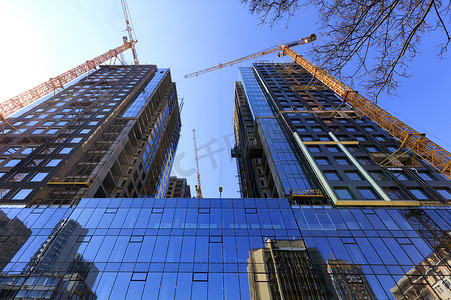 玻璃幕墙、蓝天的倒影和正在建设中的现代混凝土建筑附近的起重机。