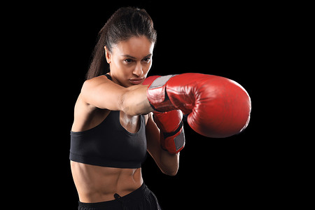 身穿运动服的跆拳道女子和黑色背景的红色跆拳道手套表演武术踢。