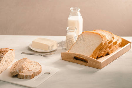 盘子架上的面包，周围是白桌上的黄油和牛奶，特写