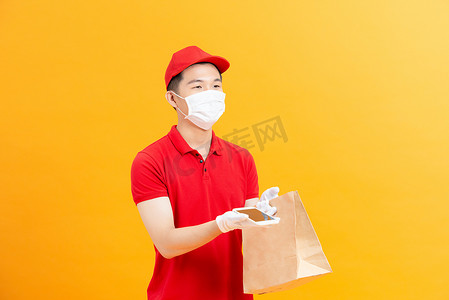 戴着医用手套和防护面罩的年轻送货员手里拿着带复印空间和购物袋的智能手机。