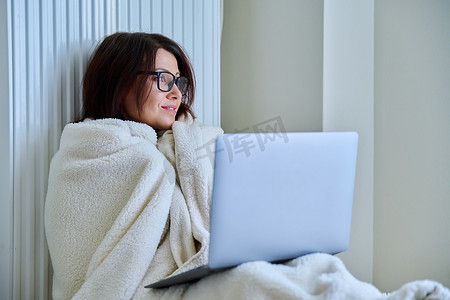 带笔记本电脑在家工作、用毯子和暖气片取暖的女性