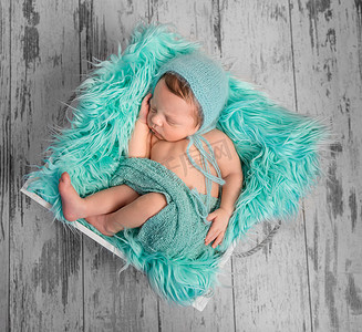 方形床上漂亮的新生婴儿，上面有毛茸茸的绿松石毯子
