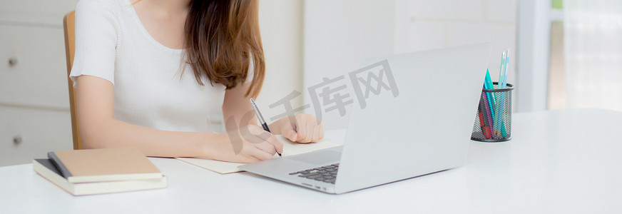 年轻的亚洲女性在笔记本上写作以计划工作和在家里的办公桌上使用笔记本电脑，关于金融、女性学习和学习、商业和沟通概念的女孩笔记。