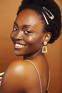年轻漂亮的非洲模特，戴着时尚风格的金色珠宝，在棕色背景下开心地笑着，生活方式人们的概念