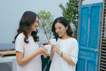 两位穿着考究的漂亮年轻女性在户外边喝咖啡边聊天