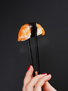 米饭筷子摄影照片_女人拿着双筷子和三文鱼寿司。