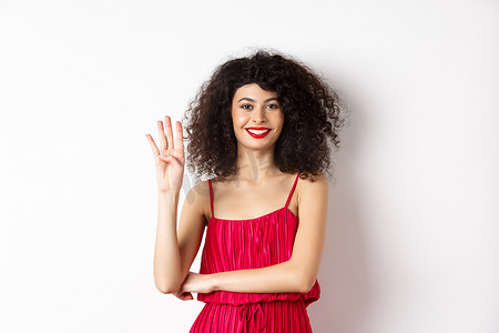 一头卷发的漂亮女模特，穿着红色连衣裙，用手指展示四号，站在白色背景下