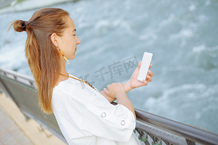 年轻女子站在路堤上用智能手机。