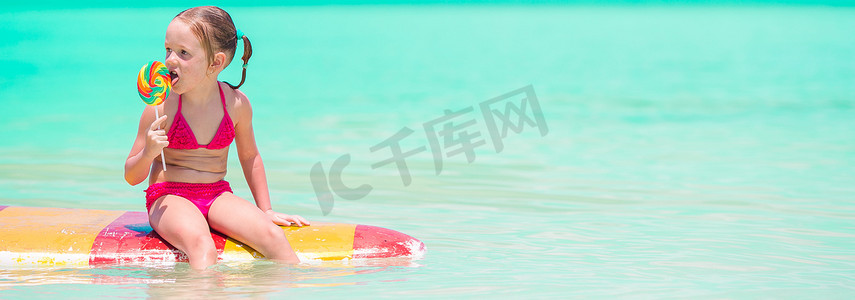 带棒棒糖的小女孩在海里的冲浪板上玩得很开心