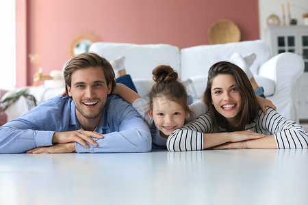 年轻的白人家庭带着小女儿在客厅的地板上放松，微笑的小女孩拥抱拥抱父母，表达爱和感激，一起在家休息。