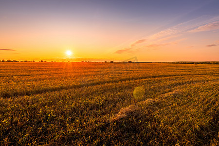 在秋天阳光明媚的夜晚，田野上的日落场景与干草堆。