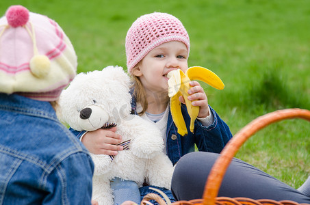 野餐的女孩吃香蕉并抱着熊
