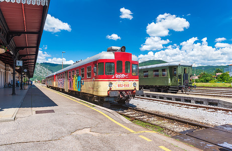 火车站背景摄影照片_新戈里察（戈里齐亚）- 2016年6月，斯洛文尼亚：老火车站铁轨上的火车广角视图，从站台上看，夏日蓝天和积云