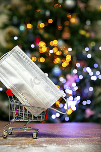 圣诞树附近铁制购物篮中的防护安全面罩、Covid-19、冠状病毒、具有复制空间和散景灯背景的假日概念