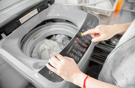 堆洗衣服摄影照片_洗衣房里的女人正在用洗衣机洗衣服。