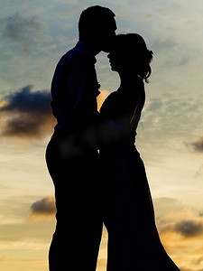 新娘和新郎在日落时接吻的剪影。